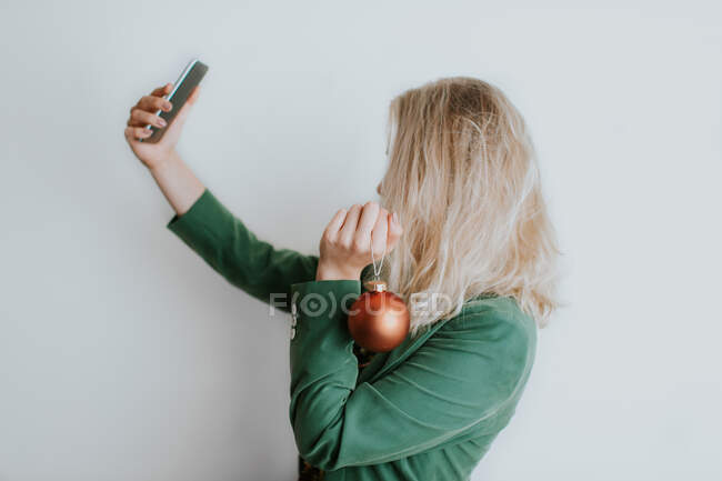 Mujer sosteniendo navidad bauble y tomando selfie - foto de stock