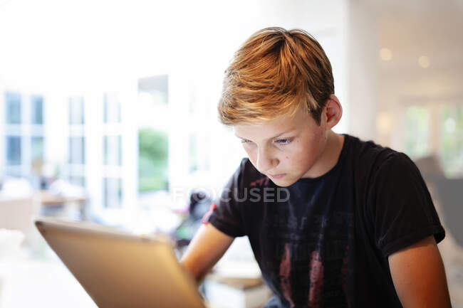 Menino sentado à mesa usando um tablet digital — Fotografia de Stock