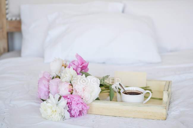 Букет півоній і чашка кави з конвертом на підносі на ліжку — стокове фото