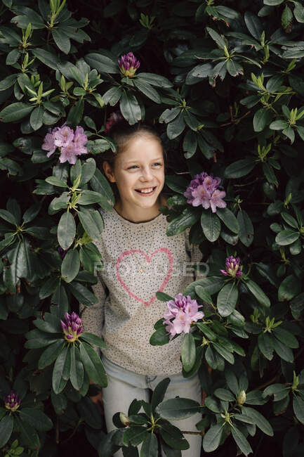 Retrato de una chica sonriente escondida en un arbusto de Rhododendron, Países Bajos - foto de stock