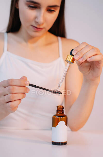 Mujer aplicando aceite a un cepillo de pestañas - foto de stock