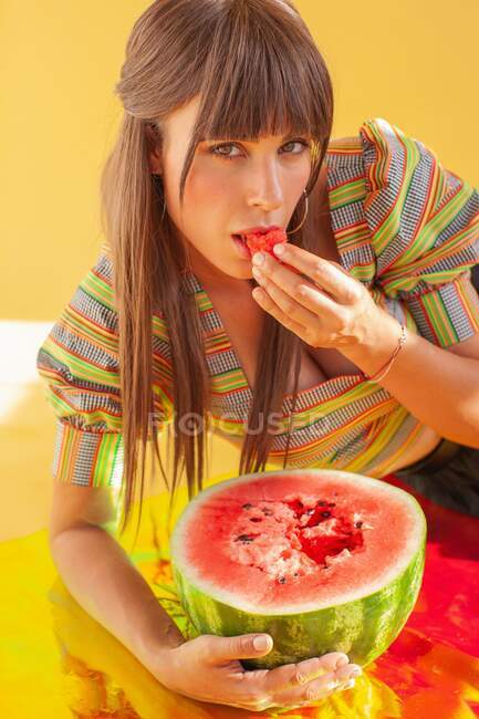Портрет усміхненої жінки, що лежить на голографічній фользі, що їсть кавун — стокове фото