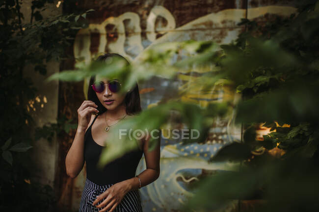 Ásia senhora vestindo óculos de sol visto através de árvore folhagem — Fotografia de Stock