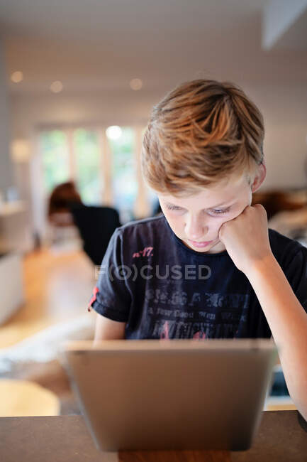 Niño sentado en la mesa usando una tableta digital - foto de stock