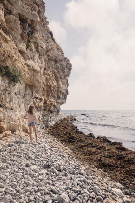 Chica de pie en la playa de guijarros con vistas al mar, Dinamarca - foto de stock