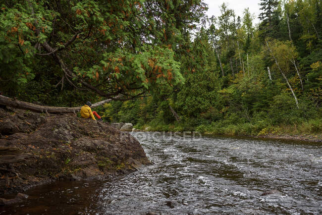 Niño sentado en las rocas junto a un río, Estados Unidos - foto de stock