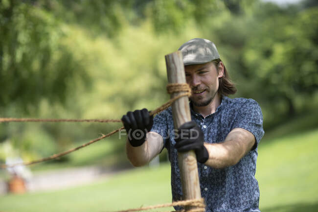 Retrato de un hombre construyendo una cerca de cuerda alrededor de plantas, Alemania - foto de stock