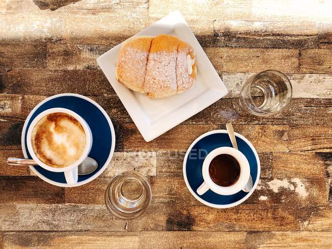 Cappuccino, espresso, agua y un croissant dulce sobre una mesa de madera - foto de stock
