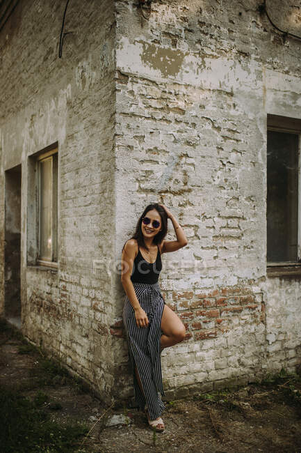 Молода стильна жінка в сонцезахисних окулярах позує на стару будівельну стіну — стокове фото