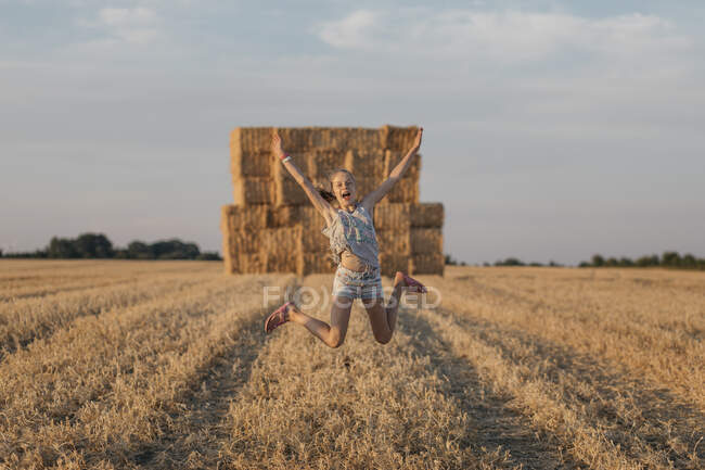Mädchen springt vor Freude auf einem Feld mit Heuballen, Dänemark — Stockfoto