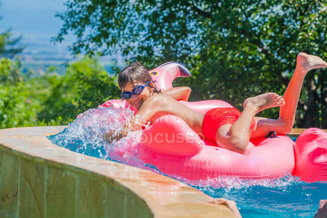 Garoto sorridente deitado em um flamingo inflável em uma piscina, Bulgária — Fotografia de Stock