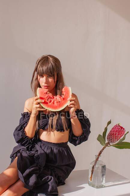 Porträt einer Frau, die neben einer Vase sitzt und eine Scheibe Wassermelone isst — Stockfoto