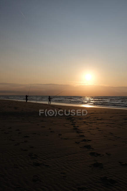 Silhouette of two people standing on beach fishing at sunset, Bleriot Beach, Pas-de-Calais, France — Stock Photo