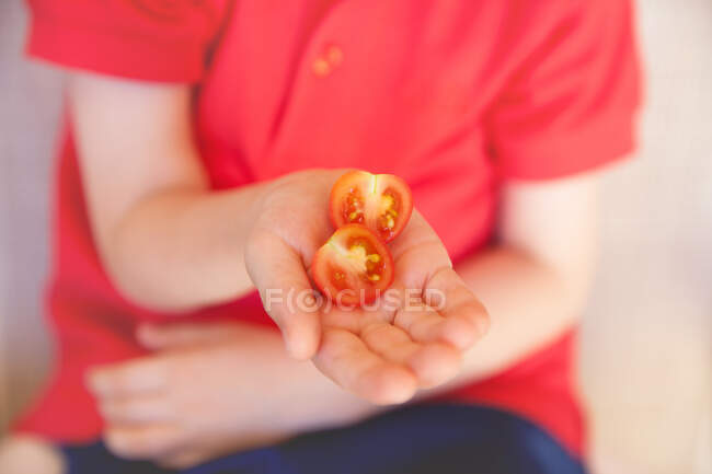 Хлопчик тримає половину вишневого помідора — стокове фото