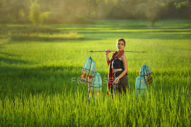 Donna in piedi in un campo che trasporta trappole per cestini, Thailandia — Foto stock