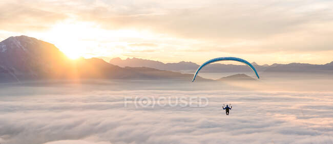 Distant view of person flying on parachute in mountainous landscape with low clouds — Stock Photo