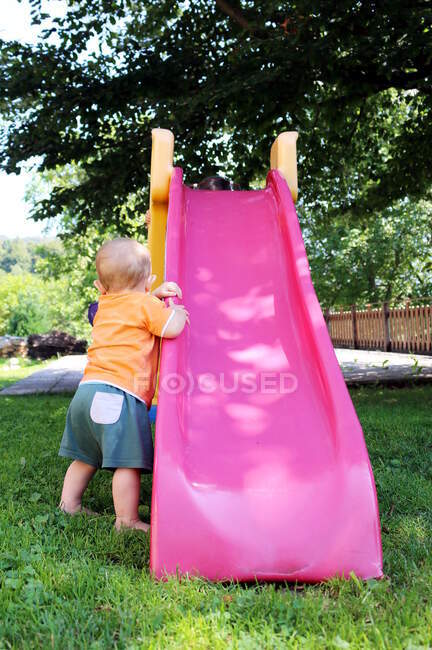Bambino in piedi in un giardino aggrappato a uno scivolo — Foto stock