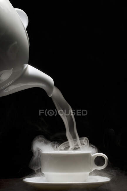 Dampf wird aus einer Teekanne in eine Teetasse gegossen — Stockfoto