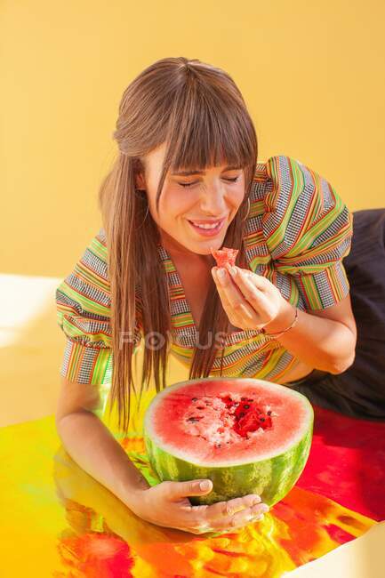 Смеющаяся женщина сидит на голографической фольге и ест арбуз — стоковое фото