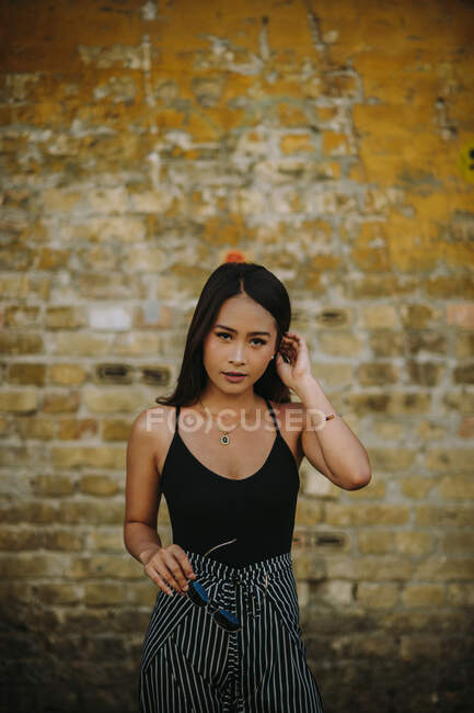 Portrait of young woman standing in front of brick wall with her hand in hair — Stock Photo