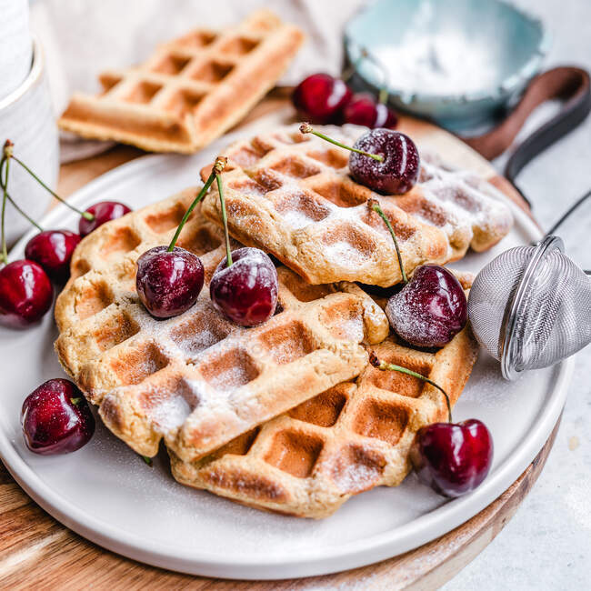 Plate of waffles with cherries and icing sugar — Stock Photo