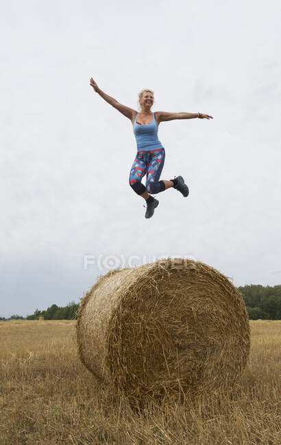 Femme sautant en l'air au-dessus d'une balle de foin, Lituanie — Photo de stock