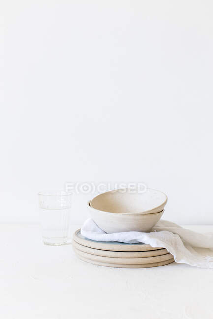 Montón de platos de cerámica y cuencos junto a un vaso de agua - foto de stock