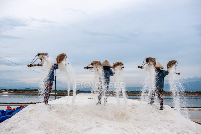 Three salt farmers standing on a pile of salt, Vietnam — Stock Photo