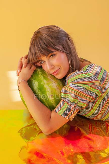 Portrait d'une femme souriante allongée sur une feuille holographique tenant une pastèque — Photo de stock