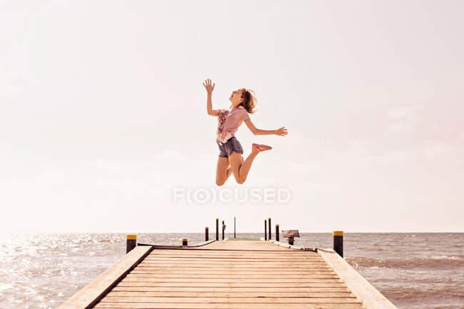 Девушка прыгает от радости на пирсе у моря, Дания — стоковое фото
