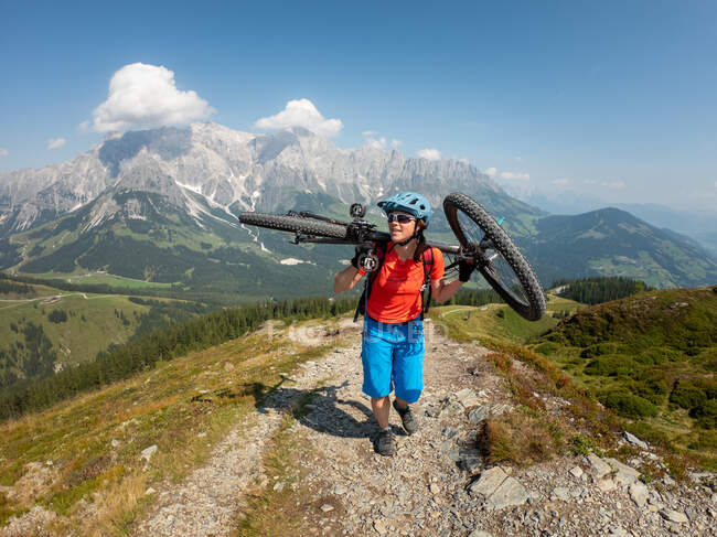 Mujer que lleva su bicicleta de montaña en un sendero alpino, Hochkoenig, Dienten, Salzburgo, Austria - foto de stock
