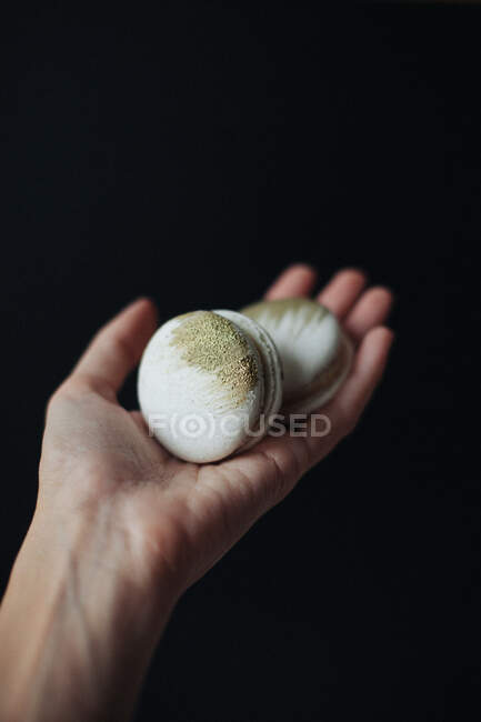 Woman's hand holding two macaroons with gold colored decoration — Stock Photo