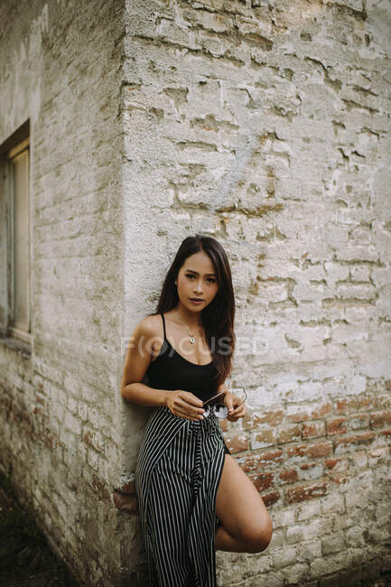 Stylish asian young woman standing by old brick wall — Stock Photo