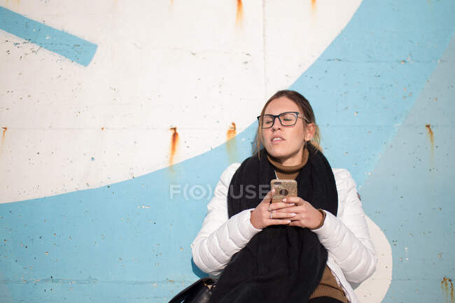 Женщина, сидящая на зимнем солнце с мобильным телефоном, Эмилия Романья, Италия — стоковое фото
