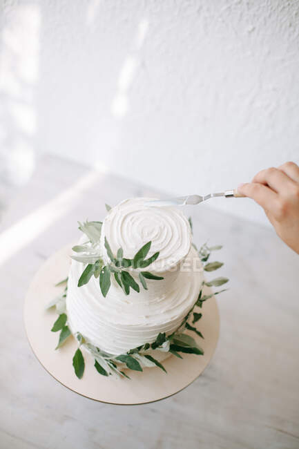 Mujer decorando un pastel de boda de dos niveles con ramas de olivo - foto de stock
