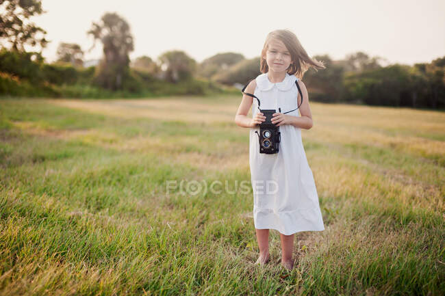 Chica de pie en un campo sosteniendo una cámara vintage, Charleston, Carolina del Sur, Estados Unidos - foto de stock