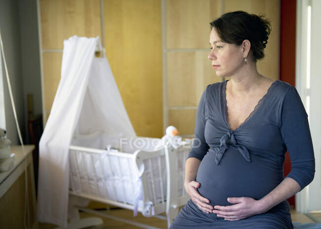 Портрет зрелой беременной женщины, сидящей рядом с пустой кроватью — стоковое фото