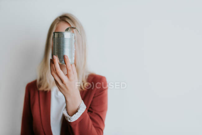 Mulher segurando lata de metal cobrindo rosto no fundo branco — Fotografia de Stock