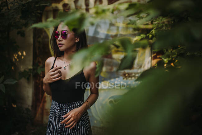 Ásia senhora vestindo óculos de sol visto através de árvore folhagem — Fotografia de Stock