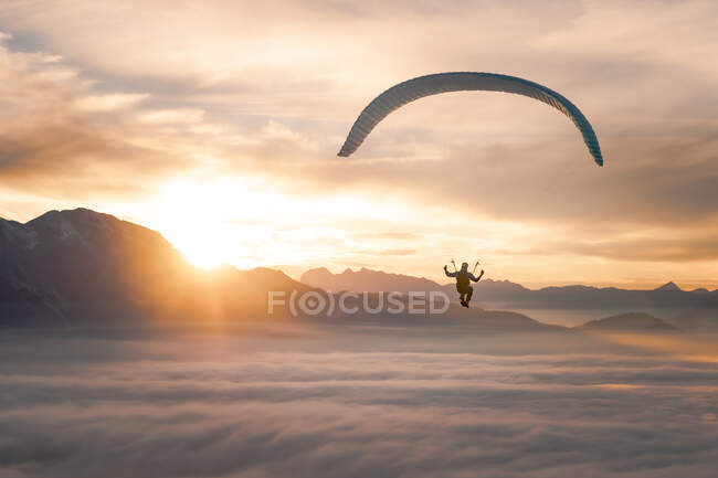Далекий взгляд на человека, летящего на парашюте в горном ландшафте с низкими облаками — стоковое фото