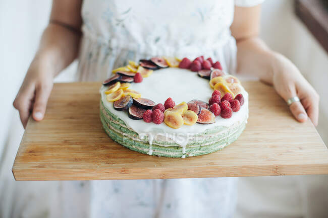 Woman carrying Homemade cake with figs and raspberries on a wooden chopping board — Stock Photo