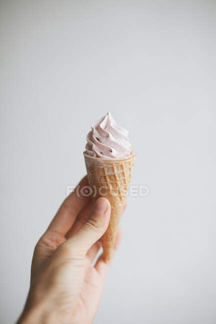 Mano de mujer sosteniendo un cono de gofre con crema batida - foto de stock