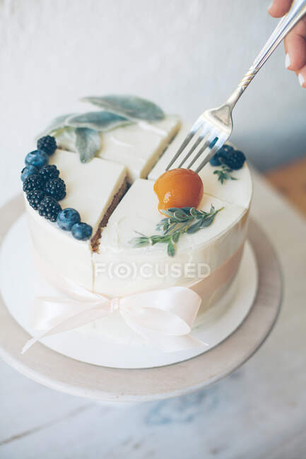 Woman eating peach off the top of a cake with buttercream icing and fruit — Stock Photo