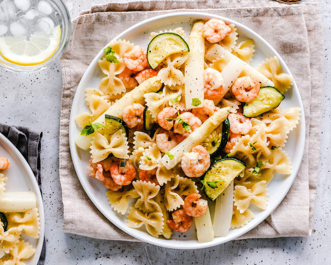 Shrimp, courgette and asparagus pasta with a glass of water — Stock Photo