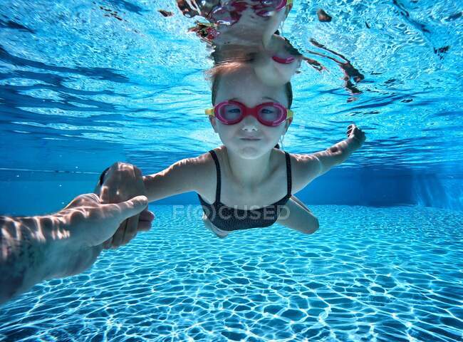 Niña nadando bajo el agua en una piscina con la ayuda de su padre - foto de stock