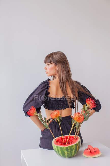 Rückansicht einer Frau, die neben einem Arrangement von Protea-Blumen in einer Wassermelone steht — Stockfoto