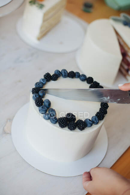 Frau schneidet Kuchen mit Blaubeeren und Brombeeren — Stockfoto