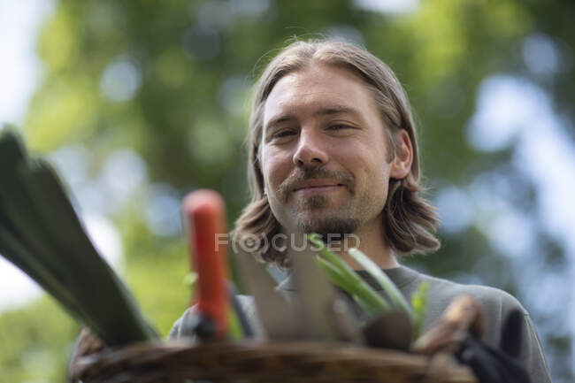 Портрет мужчины, стоящего в саду с корзиной, наполненной садовым оборудованием, Германия — стоковое фото