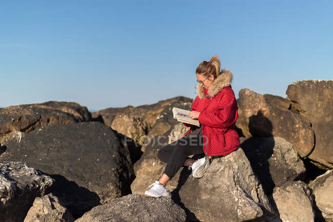 Frau sitzt auf Felsen am Meer und liest ein Buch, Emilia Romagna, Italien — Stockfoto