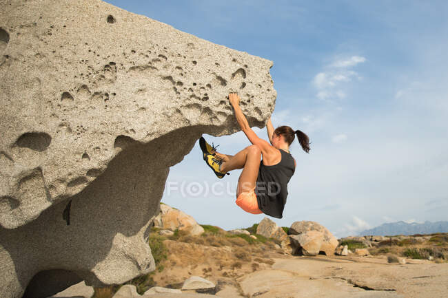 Frau klettert auf natürlichem Boulderfelsen am Strand, Korsika, Frankreich — Stockfoto